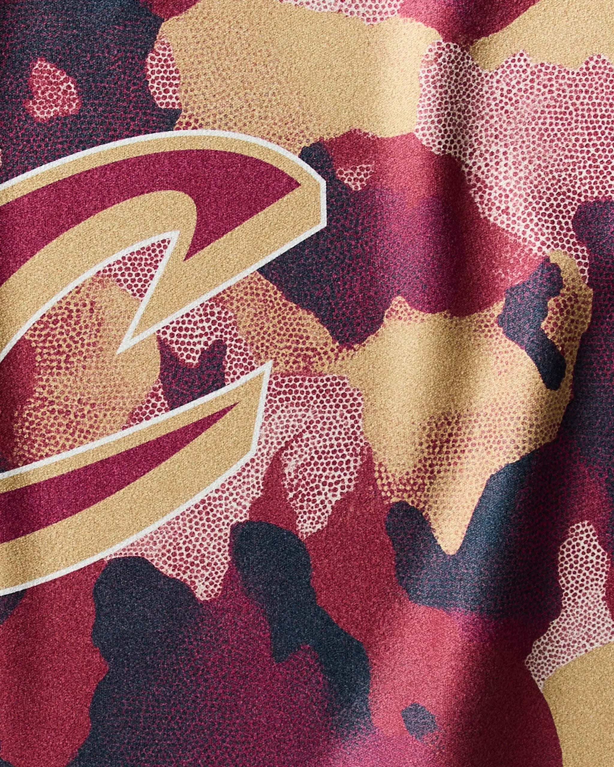 Close-up of the Geometry Cavaliers Camo fabric displaying the Cleveland Cavaliers gold C logo over a red, gold, and black camouflage pattern with a dotted texture.