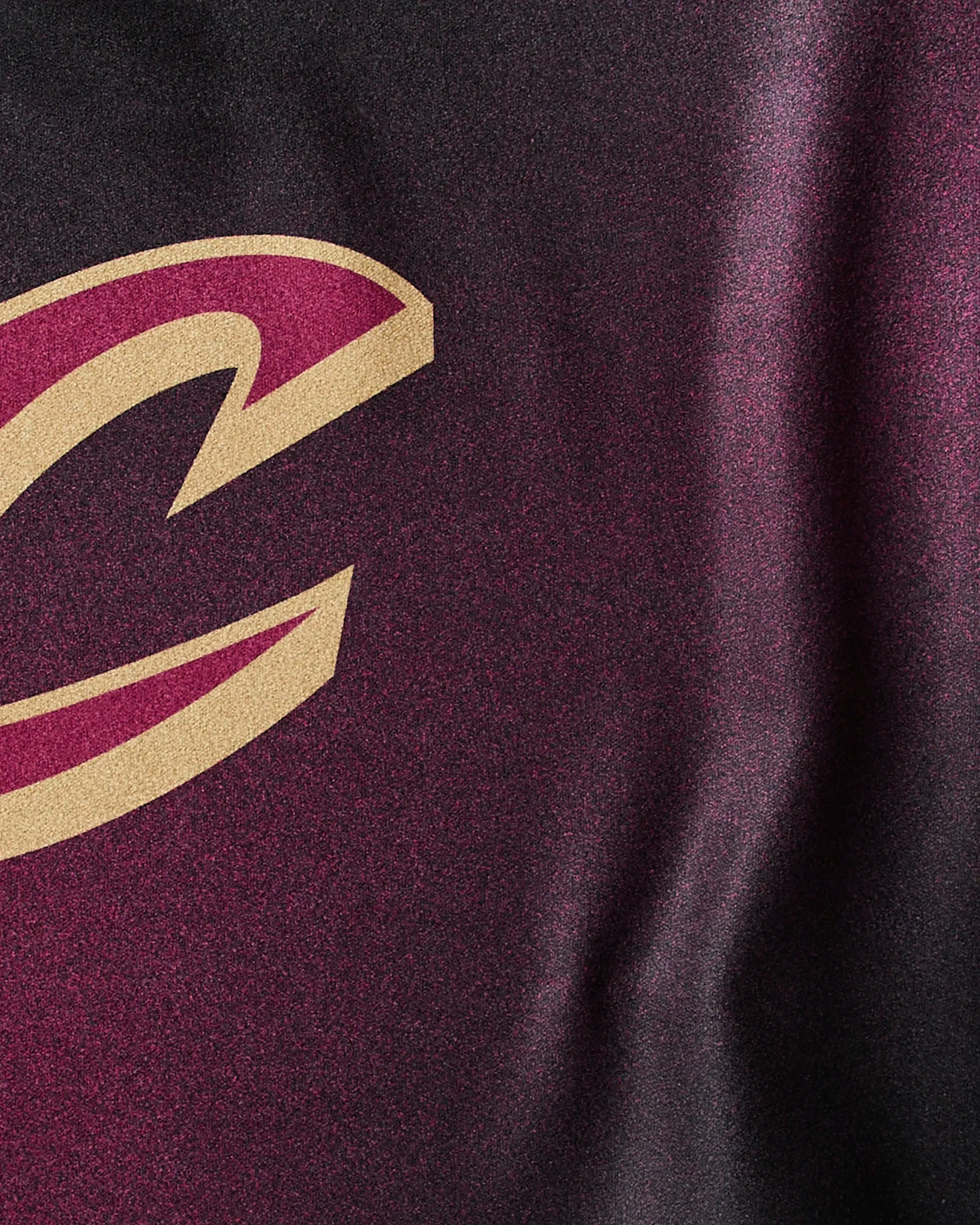 A close-up of the maroon and gold Cavaliers Fade sports jersey by Geometry, featuring part of a large, stylized C logo on textured fabric.