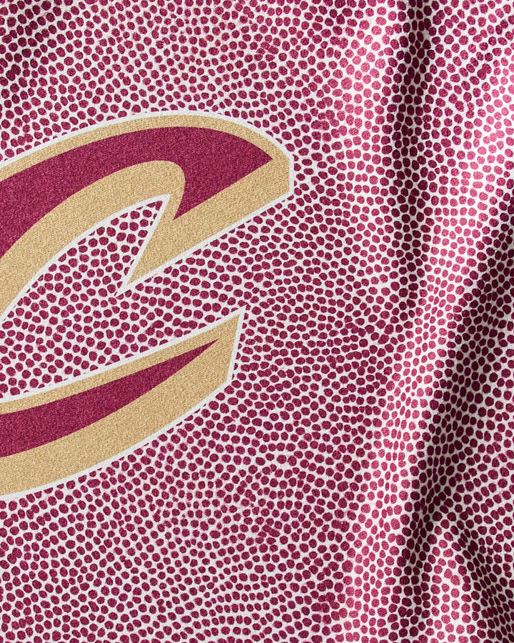 Close-up of a textured maroon surface with white dots and part of a gold-outlined maroon "C", resembling a sports jersey—perfect as the Cavaliers Grip NBA fitness towel by NBALAB x Geometry.
