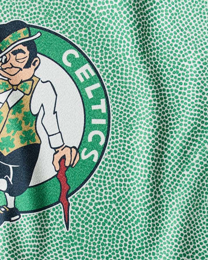 A close-up of the Boston Celtics leprechaun logo on the absorbent Celtics Grip gym towel from NBALAB x Geometry, featuring green patterned fabric in the background.