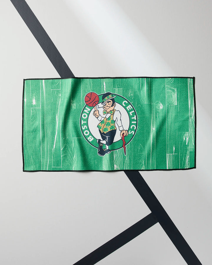 The Celtics Zone fitness towel by NBALAB x Geometry is green with the leprechaun logo and lays flat on a gray surface with black and white lines—perfect as a quick-drying gym towel for Boston Celtics fans.