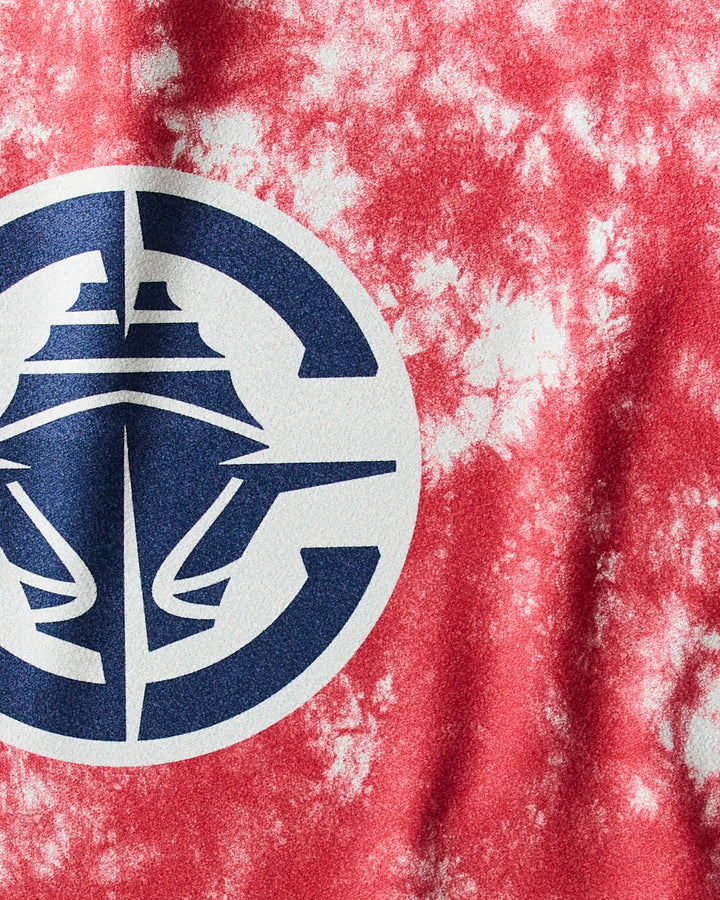A close-up of the Clippers Flash Geoweave fabric by NBALAB x Geometry shows red and white tie-dye with a bold navy and white graphic resembling a stylized ship’s bow inside a circle.