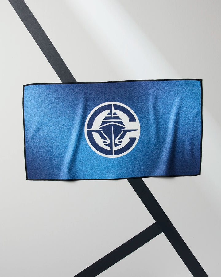 The Clippers Fade by NBALAB x Geometry is a blue rectangular quick-dry gym towel with a circular white logo of a stylized ship and wings, shown against a white wall with diagonal black lines.