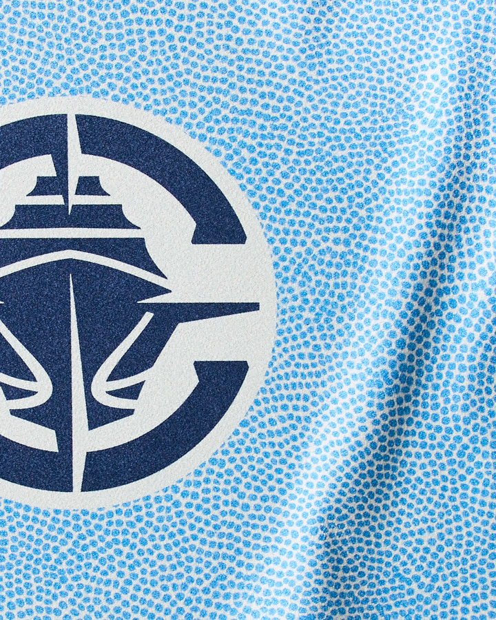 Close-up of the Clippers Grip NBA fitness towel by NBALAB x Geometry, showcasing a blue and white patterned fabric with a dark blue circular ship logo, accented by small blue dots on a light blue background.
