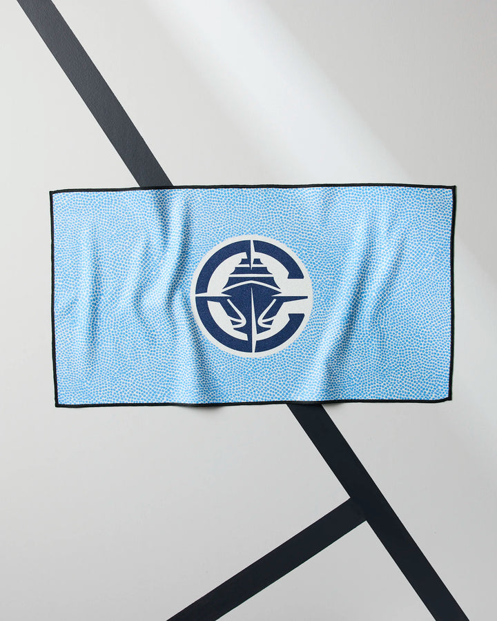 A light blue Clippers Grip gym towel by NBALAB x Geometry, featuring a dotted pattern and a dark blue ship logo in a circular emblem, laid flat on a white surface with diagonal black lines.