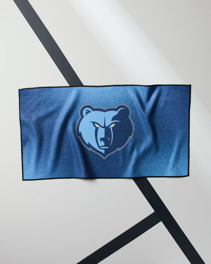 The Grizzlies Fade gym towel by NBALAB x Geometry is blue, rectangular, quick-drying, and features a fierce grizzly bear head logo with yellow eyes on a light gray background with black diagonal lines.