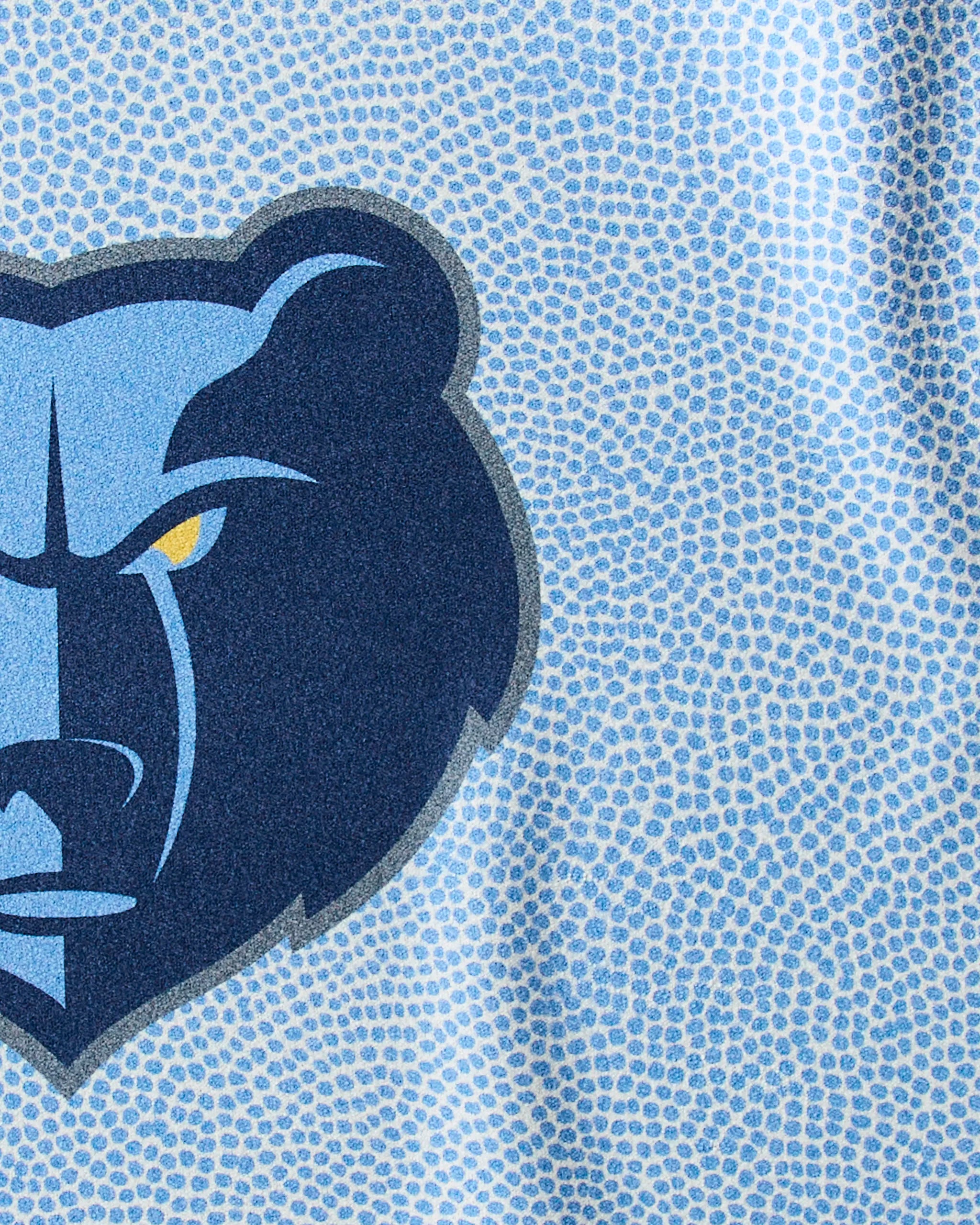 Close-up of the stylized blue Grizzlies Grip bear head logo with a stern look on a light blue, dotted background, featured on Geometry's NBA fitness towel designed for durability and quick-drying during workouts.