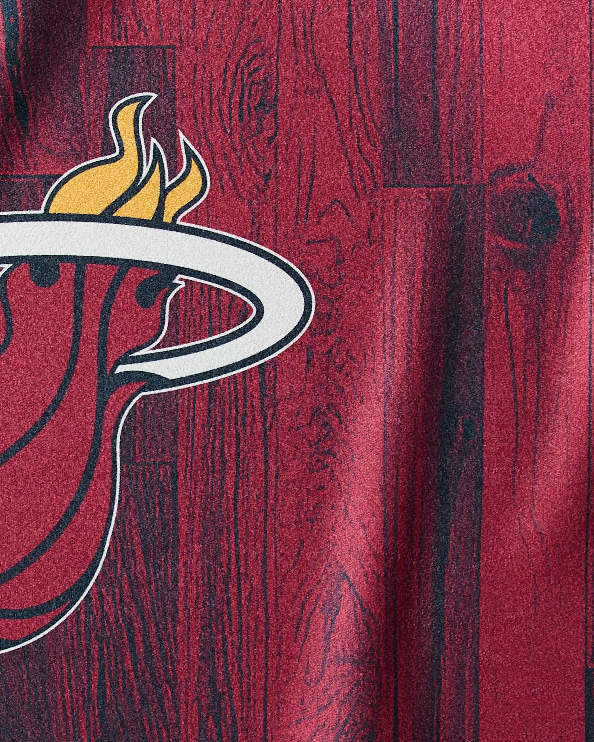 Close-up of the Heat Zone towel by Geometry, showing a red and black surface with part of the Miami Heat logo—a flaming basketball through a white hoop on wood-patterned background—perfect NBA fitness inspiration.