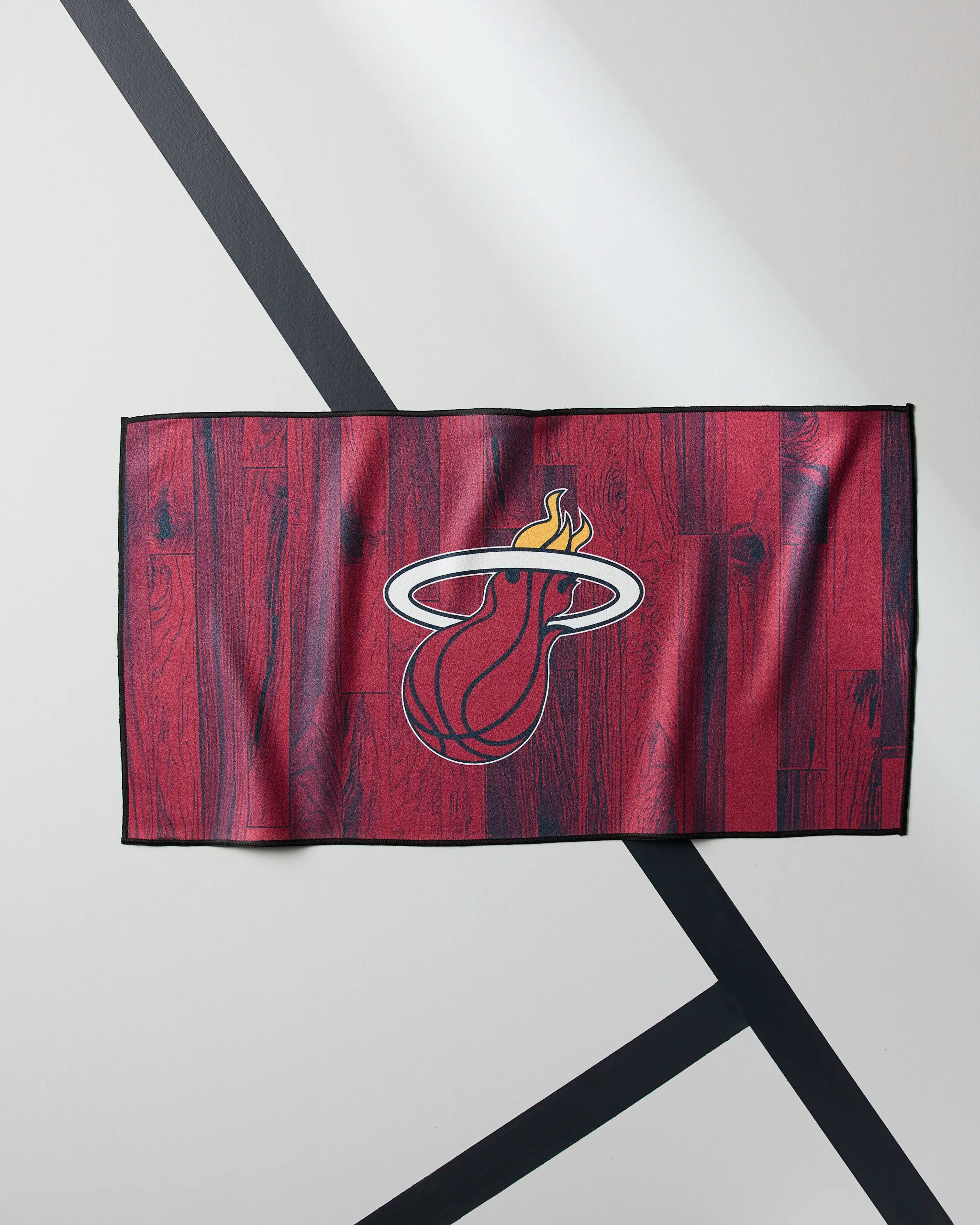 The Geometry Heat Zone towel features a red NBA design with a woodgrain pattern and the Miami Heat's flaming basketball logo—laid flat on a white surface with black lines, it's your ideal workout companion.