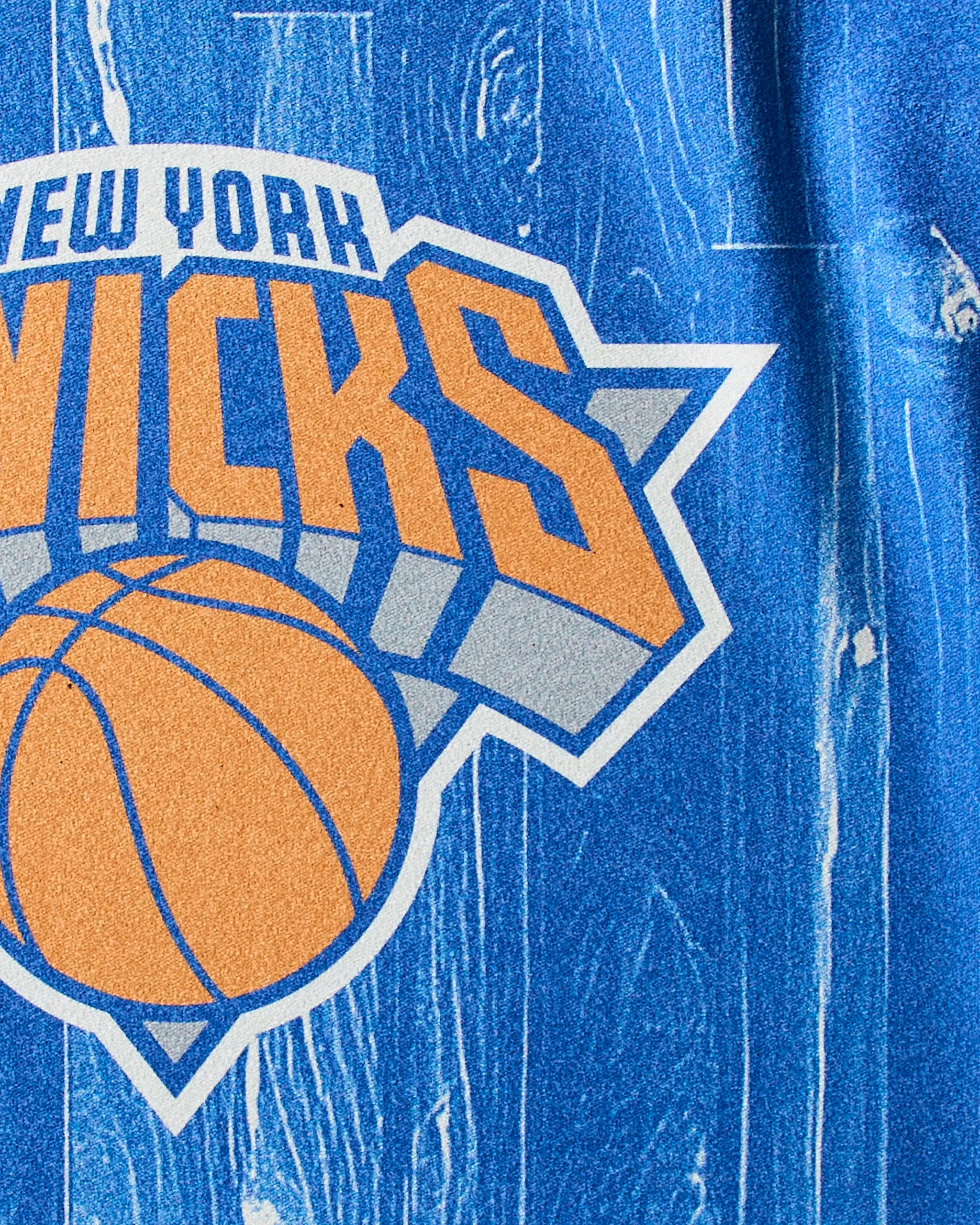 Close-up of the Knicks Zone logo by Geometry on a blue, textured NBA fitness towel, featuring "Knicks" in bold above an orange basketball.