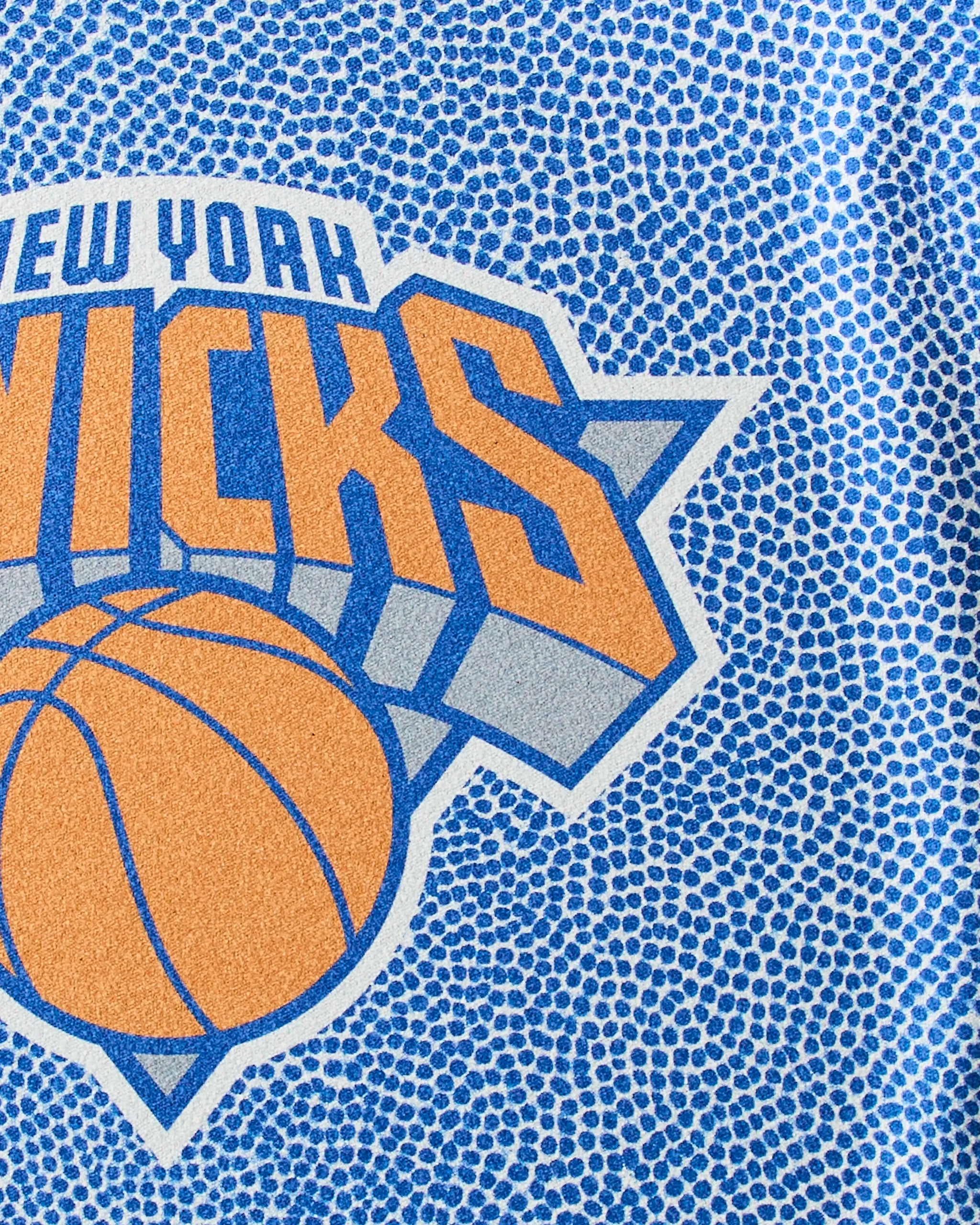 Close-up of the Knicks Grip by Geometry: a quick-drying workout towel with a textured, basketball-like blue background and bold orange Knicks logo—perfect for any NBA fan’s gym bag.