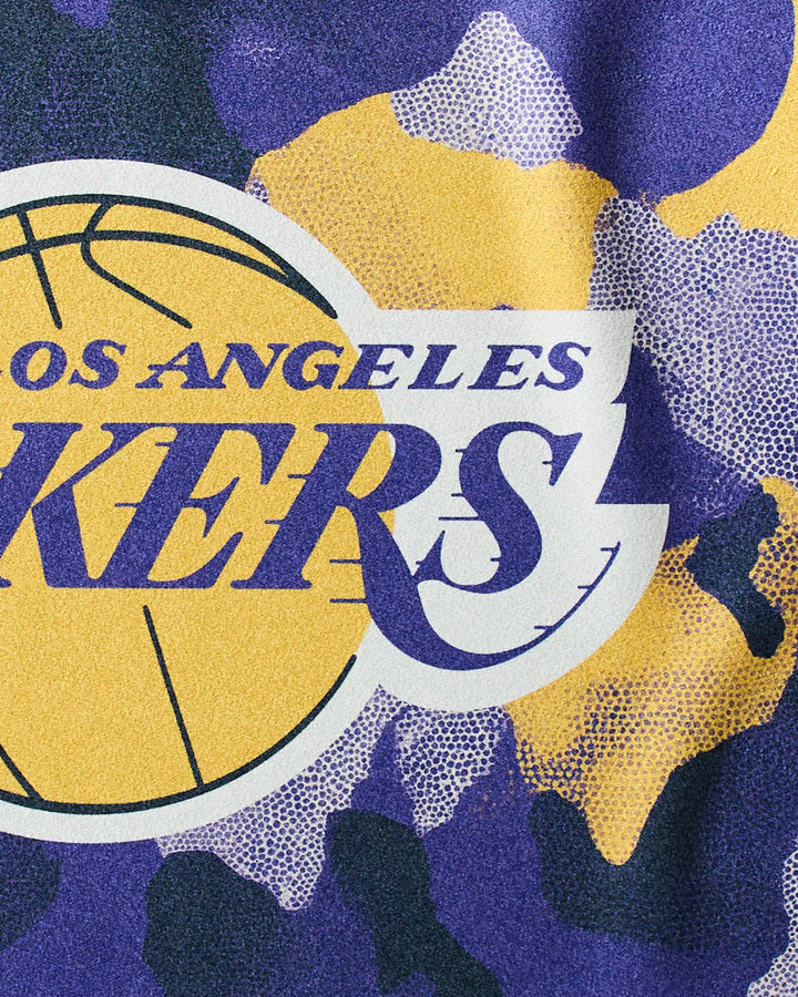Close-up of the NBALAB x Geometry Lakers Camo fitness towel, featuring a Los Angeles Lakers logo on a yellow, purple, and white camo background. Made with sustainable Geoweave fabric, it displays bold team lettering and part of a basketball.