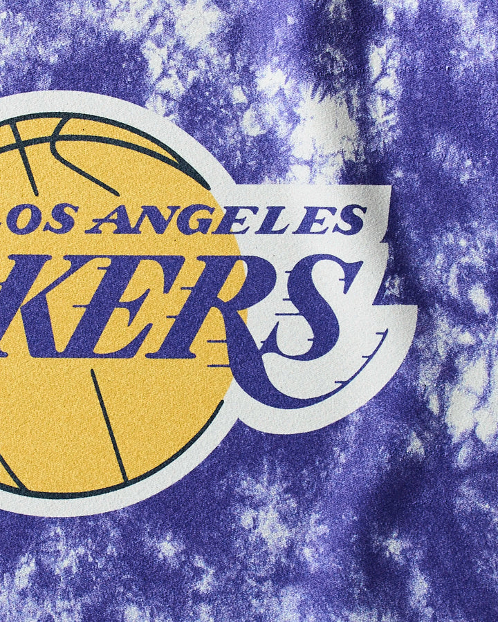 Close-up of the NBALAB x Geometry Lakers Flash fitness towel, featuring the Los Angeles Lakers logo on a purple and white tie-dye design with part of a yellow basketball and bold purple text.