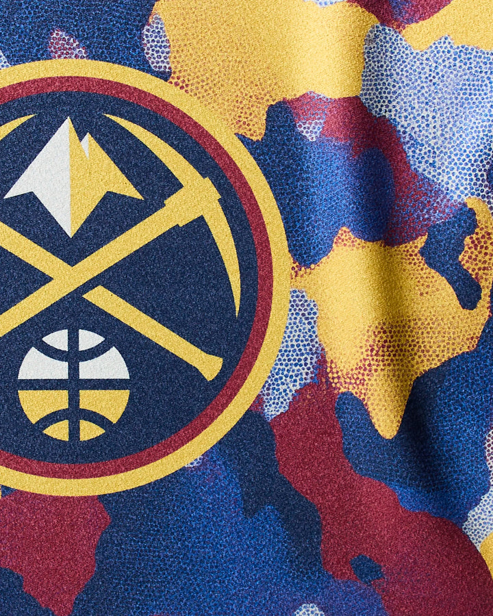 Close-up of the NBALAB x Geometry Nuggets Camo towel shows the Denver Nuggets logo with pickaxe and mountain on a blue, yellow, red, and white abstract background—perfect for fans or as an NBA licensed fitness towel.