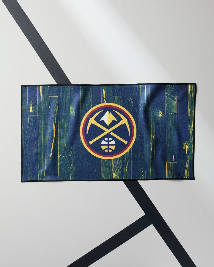The NBALAB x Geometry Nuggets Zone fitness towel, in navy and gold with the Denver Nuggets logo, lies flat on a light gray surface with black lines—melding team pride and quick-drying gym performance.