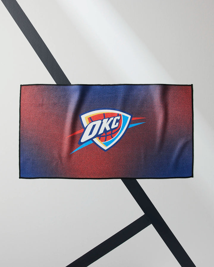 The OKC Fade by NBALAB x Geometry is a rectangular fitness towel with the Oklahoma City Thunder logo on a red and blue gradient, shown on a white surface with black diagonal lines.