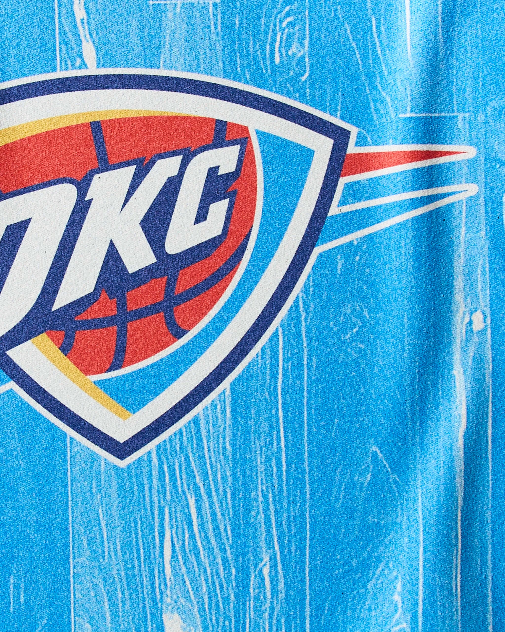 Close-up of the Oklahoma City Thunder logo on a textured blue, wood grain-like background, featured on the Geometry OKC Zone quick-drying workout towel.