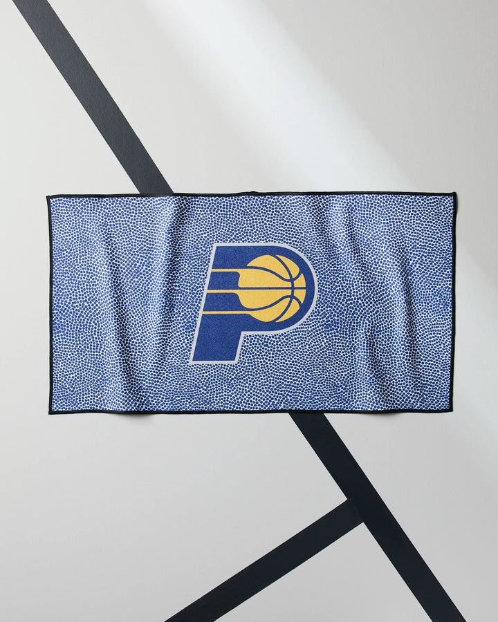 The Pacers Grip by NBALAB x Geometry is a blue NBA fitness towel with a speckled pattern, featuring the Indiana Pacers logo—a stylized P with a yellow basketball—on a white background with diagonal black lines.