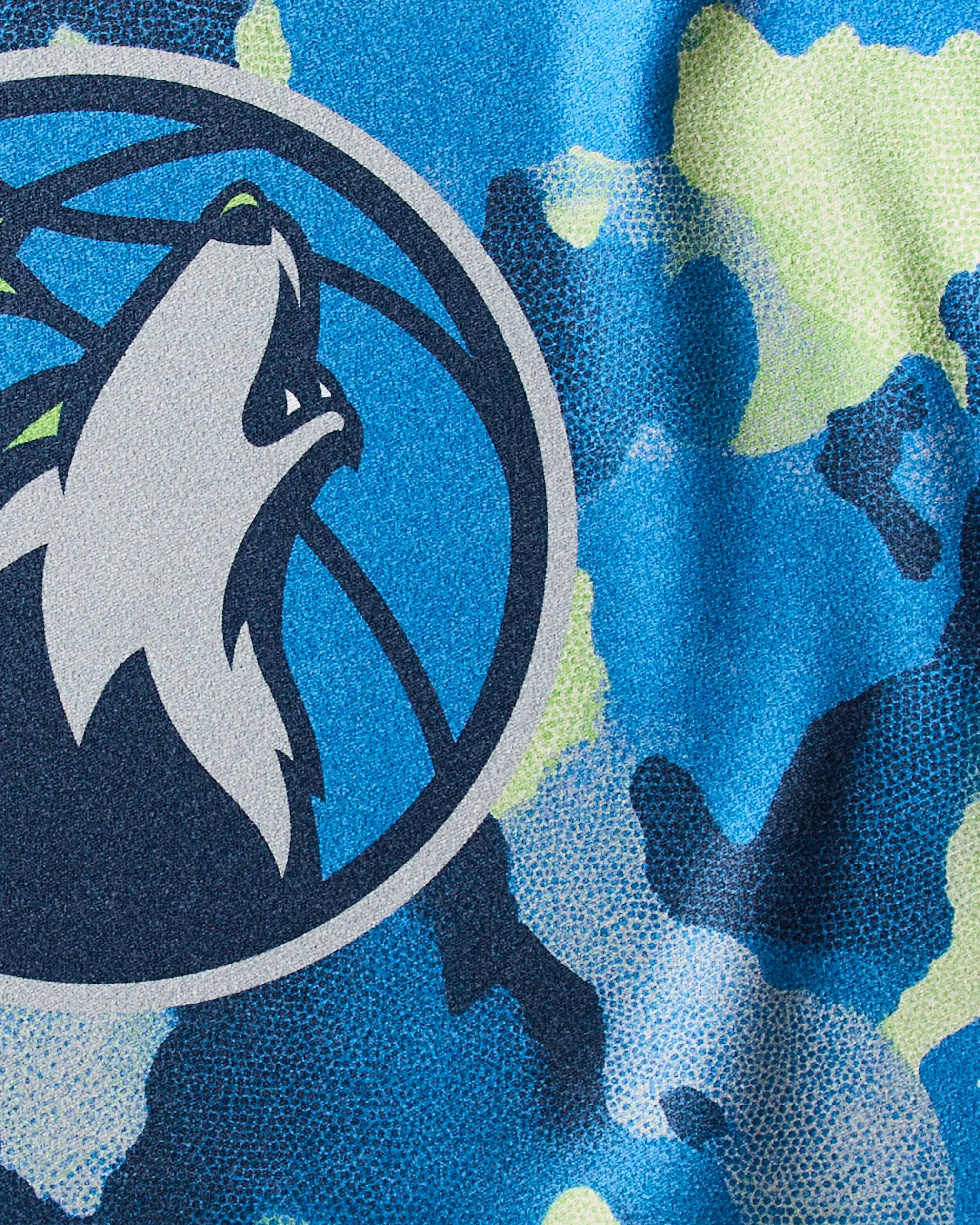 The Geometry Timberwolves Camo towel features a close-up of the Minnesota Timberwolves logo with a stylized wolf head on a blue, green, and navy camo background—perfect for quick-drying after tough workouts.