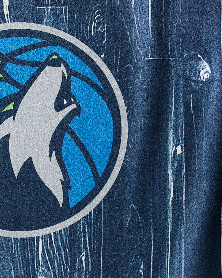 Close-up of the Timberwolves Zone logo—a wolf howling at a blue basketball—printed on the NBALAB x Geometry dark textured NBA fitness towel, perfect for fans to display team pride during every workout.