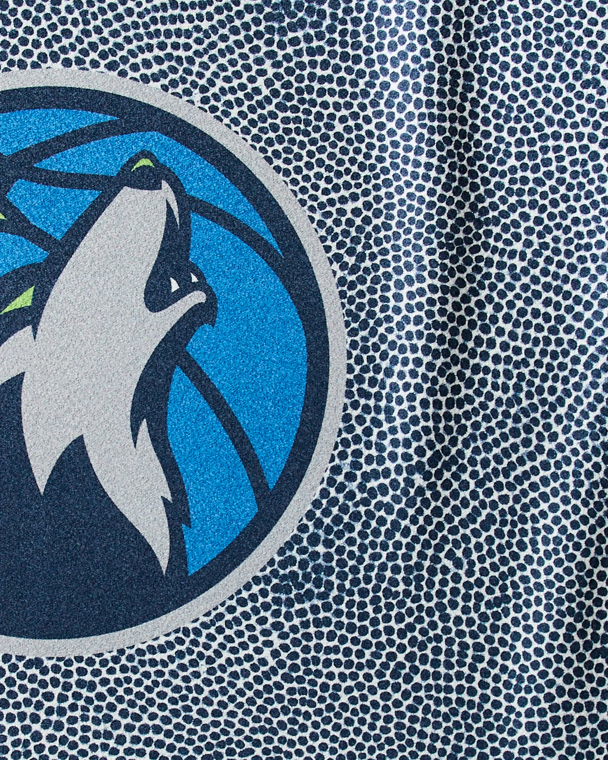 Close-up of the Geometry Timberwolves Grip fitness towel, featuring a basketball texture and the Minnesota Timberwolves logo—a stylized wolf head in white, gray, and blue inside a blue basketball circle.