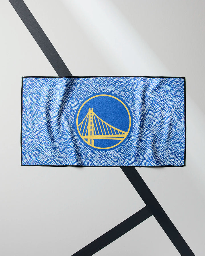 The NBALAB x Geometry Warriors Grip is a blue rectangular quick-drying gym towel with a yellow bridge logo in a blue circle outlined in yellow, black borders, and displayed on a white surface with black diagonal lines.