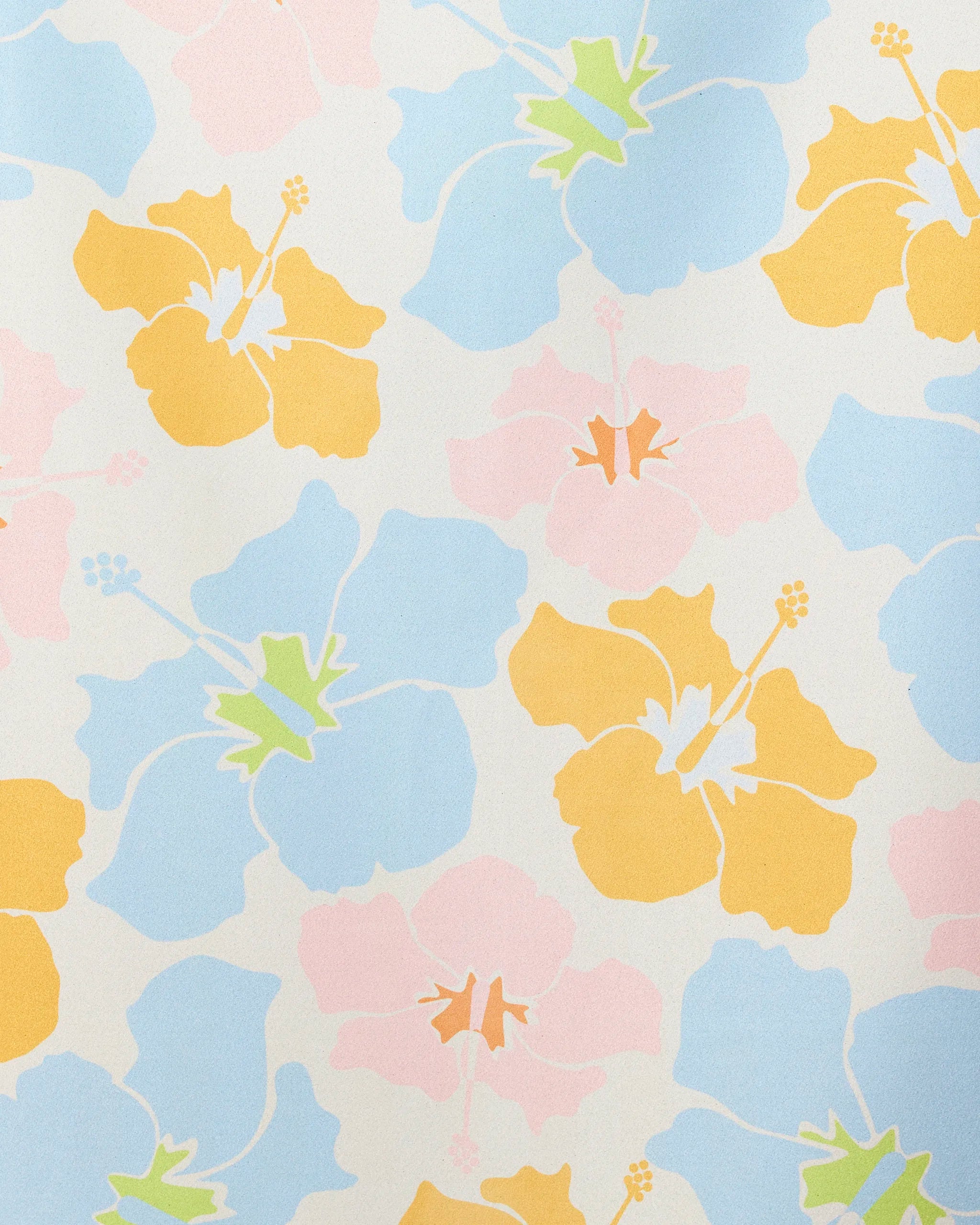 The GEOMETRY Hula Hues towel features a seamless pattern of large yellow, blue, and pale pink hibiscus flowers with light green accents on an off-white background for a bright, airy vintage tropical look. Quick-drying design.