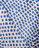 The Shelly Back quick-drying beach towel by GEOMETRY features a dynamic geometric design of blue squares in diagonal, wavy lines on a light beige background.