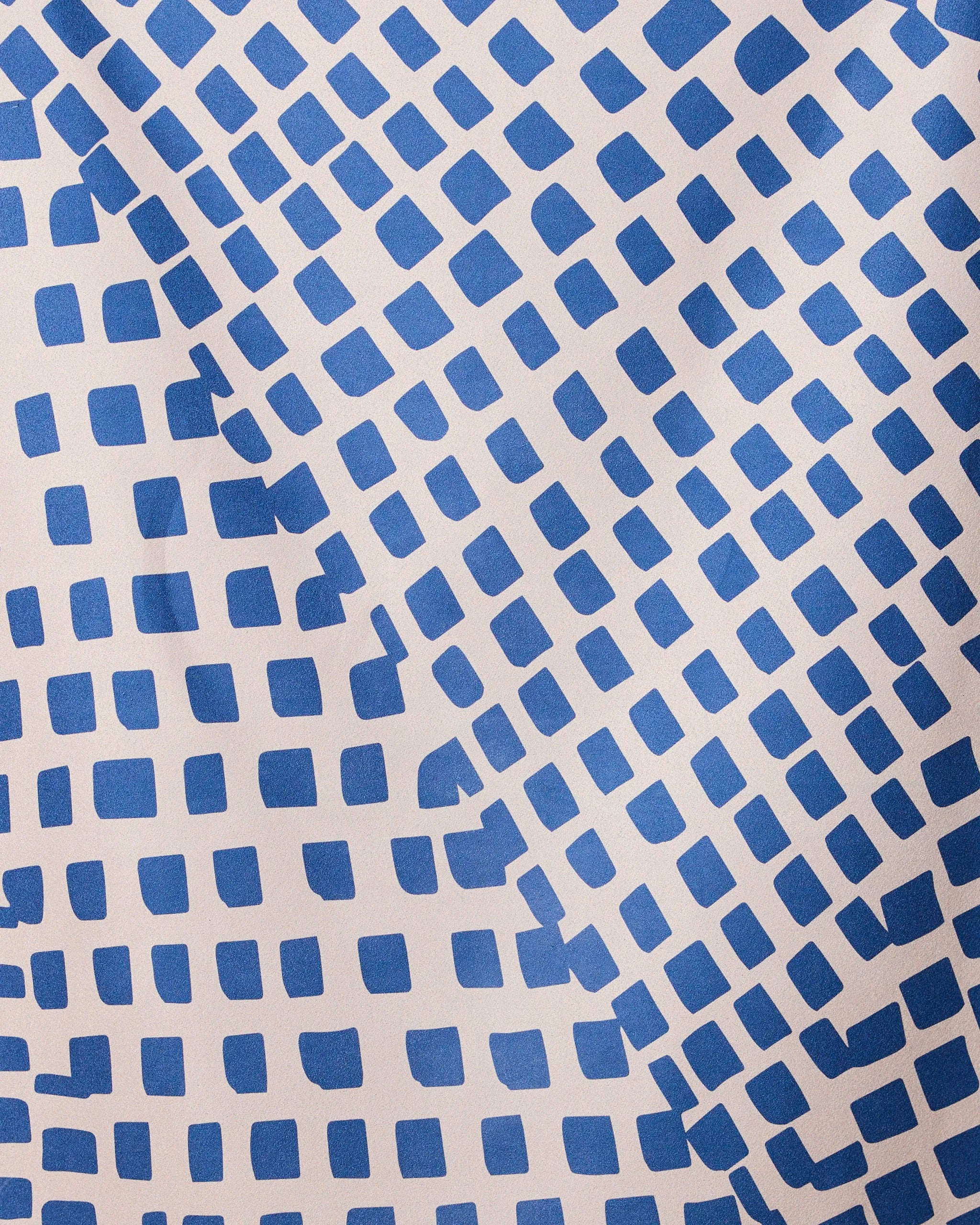 The Shelly Back quick-drying beach towel by GEOMETRY features a dynamic geometric design of blue squares in diagonal, wavy lines on a light beige background.