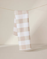 The GEOMETRY Betty Bakes eco-friendly kitchen towel in beige and white checkered design hangs neatly over a thin clothesline, set against a softly lit neutral background.