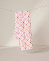 The GEOMETRY Anew tea towel features a quick-drying design with a pink and orange geometric crisscross pattern and small purple dots, shown hanging by a string against a neutral background.