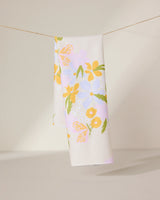 The GEOMETRY Abloom tea towel, made from ultra-absorbent recycled materials, features a white background with yellow, orange, and purple flowers and green leaves—perfect for brightening any kitchen.
