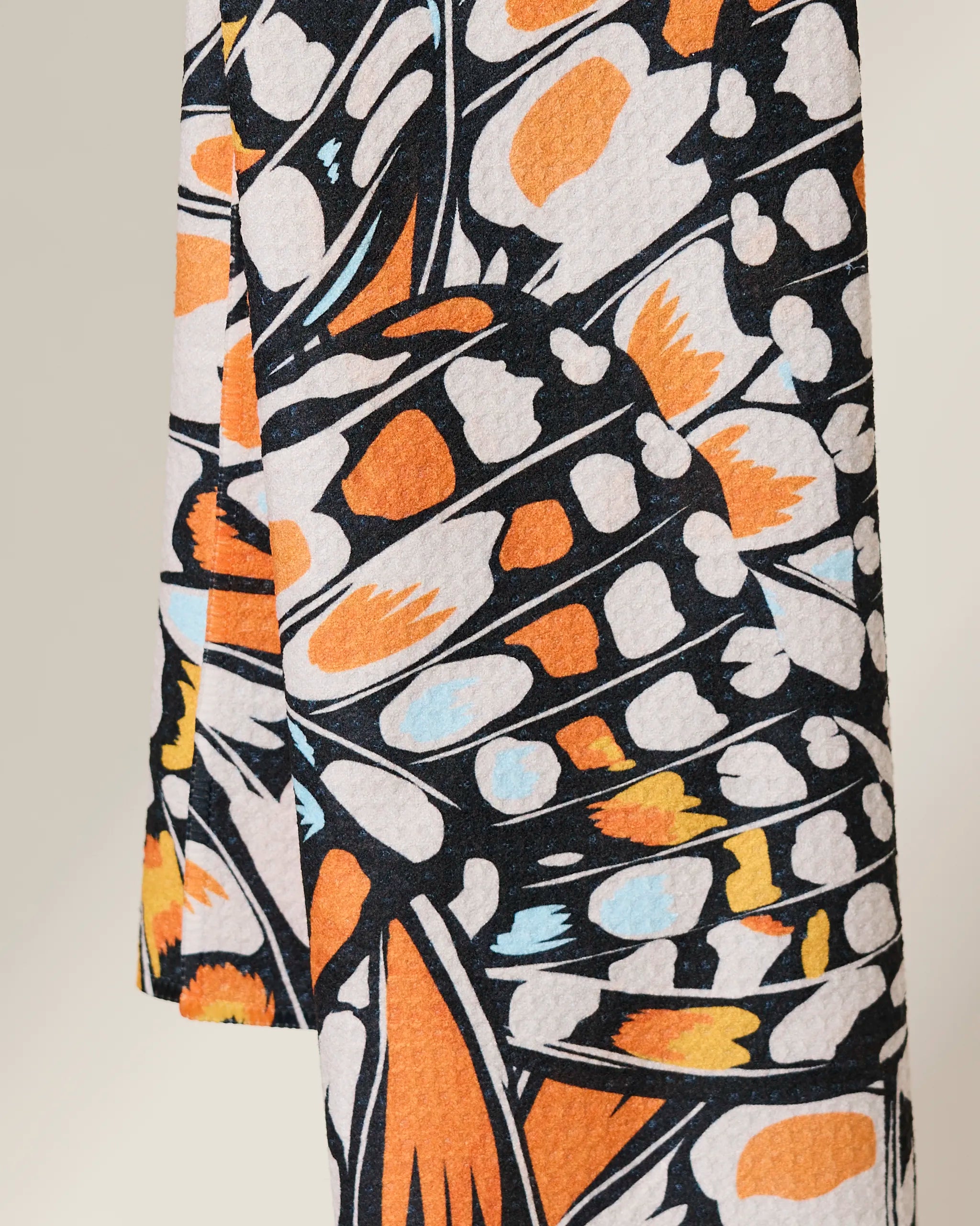 Close-up of GEOMETRYs Wings in the Wind towel, an ultra-absorbent piece featuring a vibrant abstract butterfly wing pattern in orange, black, white, and light blue. The textured fabric drapes beautifully to showcase its striking design.