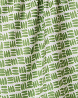 A close-up of the GEOMETRY Grass Hatch tea towel shows its ultra-absorbent white fabric with a repeating pattern of short green hand-drawn lines and ovals in horizontal rows, creating gentle folds and subtle shadows.