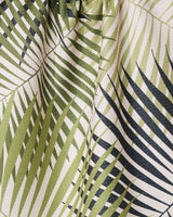 Close-up of GEOMETRY’s Green Fronds eco-friendly tea towel, featuring overlapping green palm leaves on a light background, with visible creases and textured material.