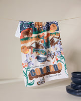Geometry’s “Greetings From Colorado” tea towel, quick-drying and colorful, hangs by blue dishes. It features Colorado wildlife, mountains, flowers, and “Greetings from Colorado, The Centennial State.”.
