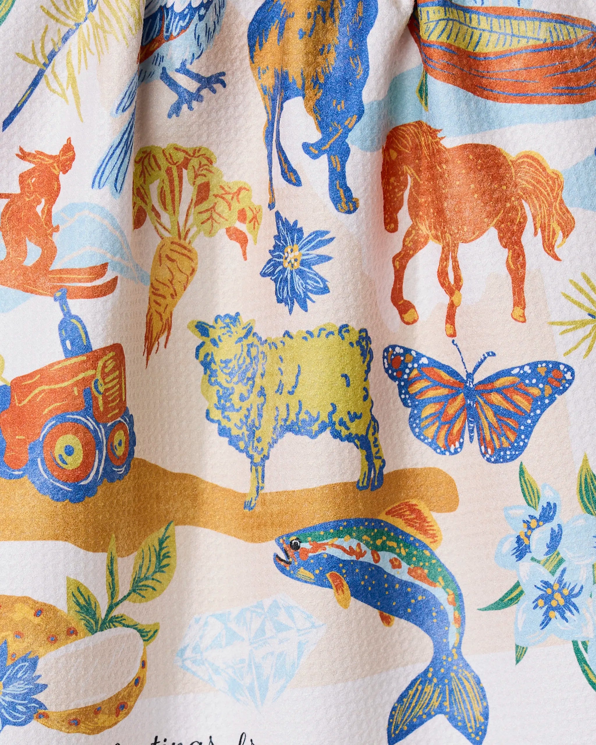 The Geometry Greetings From Idaho Kitchen Tea Towel features Geoweave fabric with blue, orange, and yellow animal illustrations—horse, sheep, cat, butterfly, fish—on a light background.