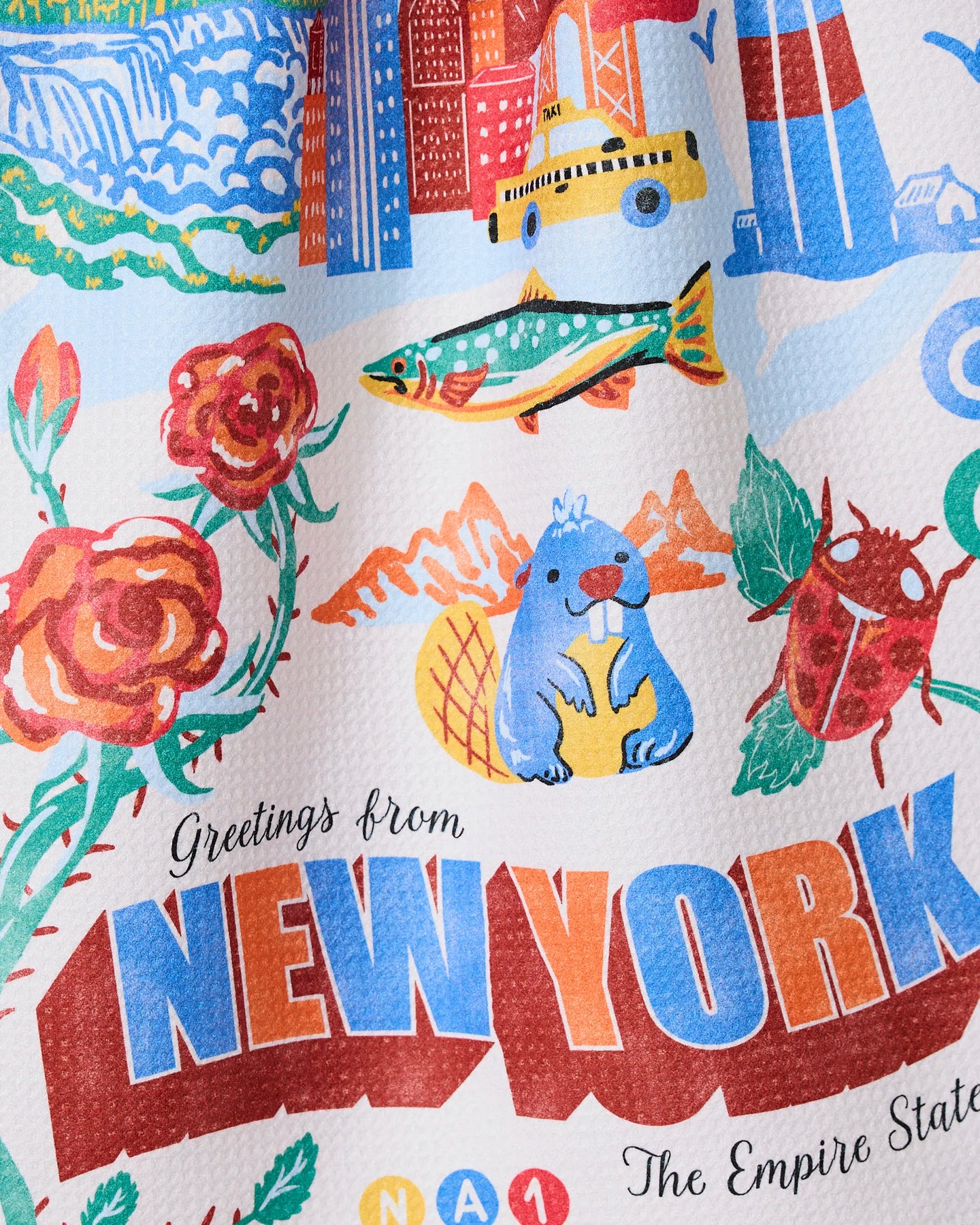 The Geometry Greetings From New York kitchen towel features a colorful illustration with red roses, a fish, blue beaver, beetle, and the NYC skyline, plus Greetings from NEW YORK and The Empire State at the bottom.