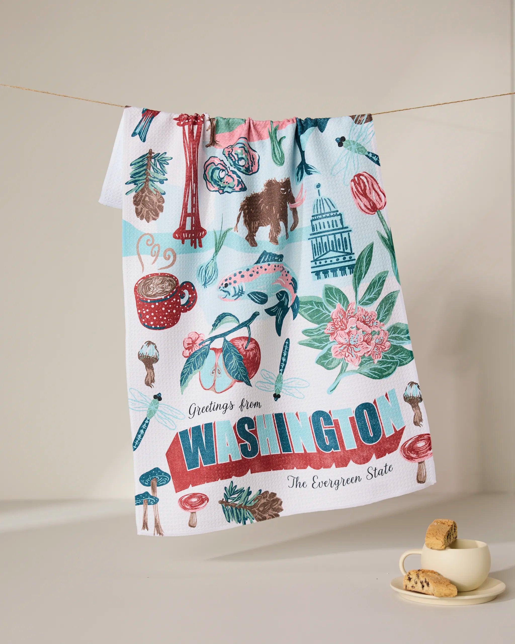 The Geometry Greetings From Washington tea towel, made from recycled materials, features vibrant state icons like the Space Needle, coffee, and apples—an ultra-absorbent kitchen essential.