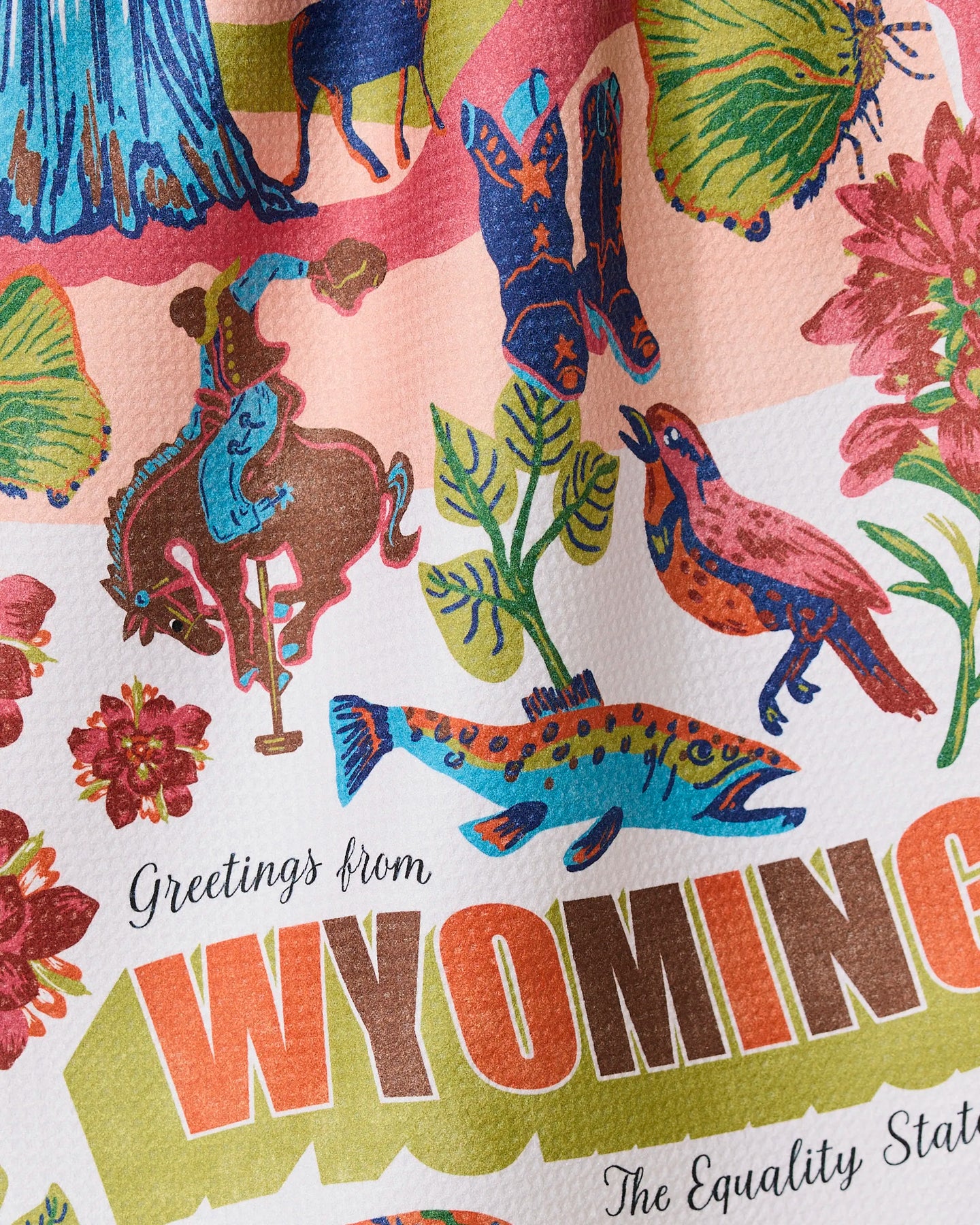 The Geometry Greetings From Wyoming ultra-absorbent towel showcases a colorful cowboy, horse, flowers, bird, fish, and the text Greetings from WYOMING with The Equality State on a textured background.