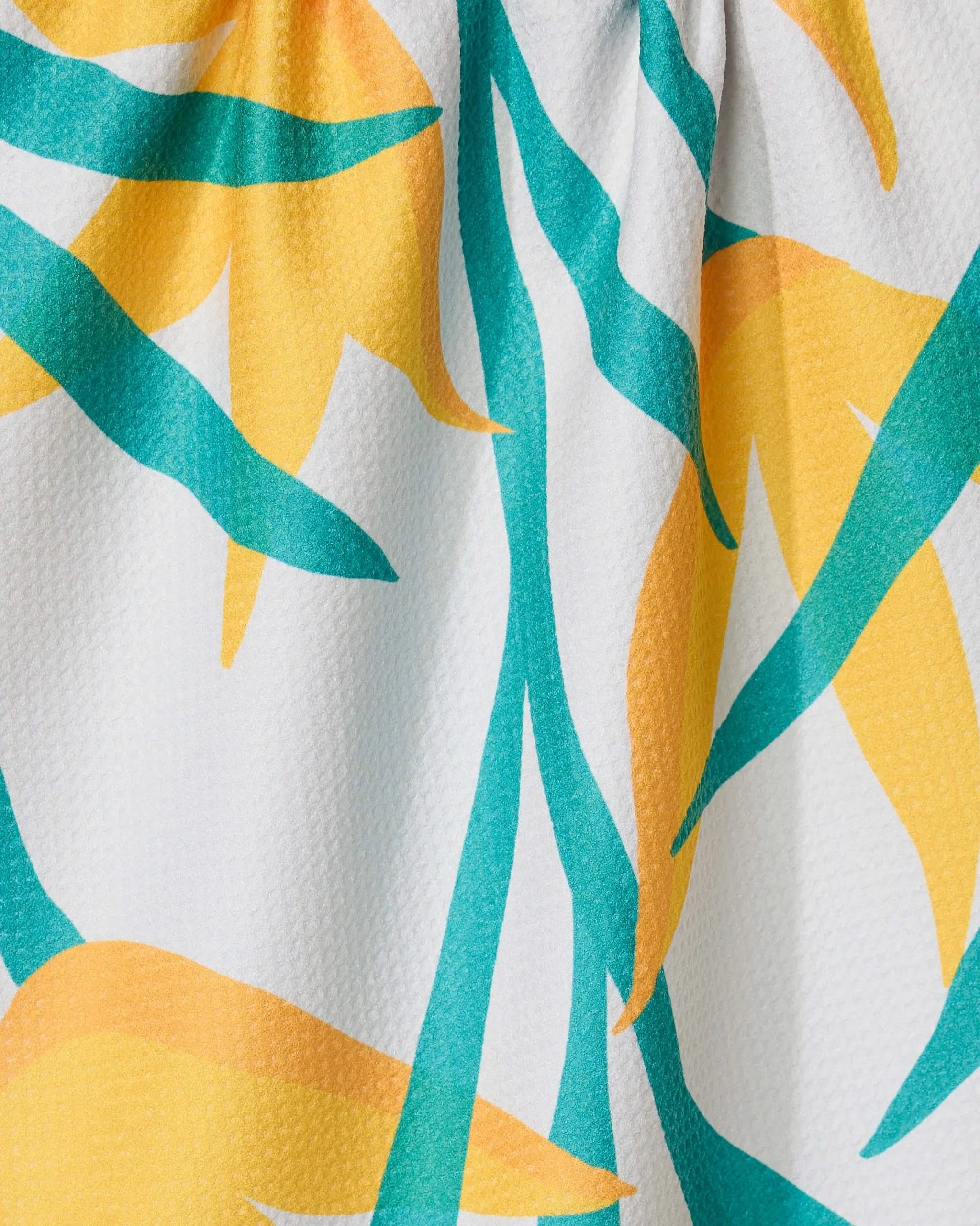 Close-up of GEOMETRYs Growth kitchen tea towel, featuring a tropical print with yellow and orange abstract flowers, teal green leaves on a white textured background. Made with Geoweave technology for superior absorbency.