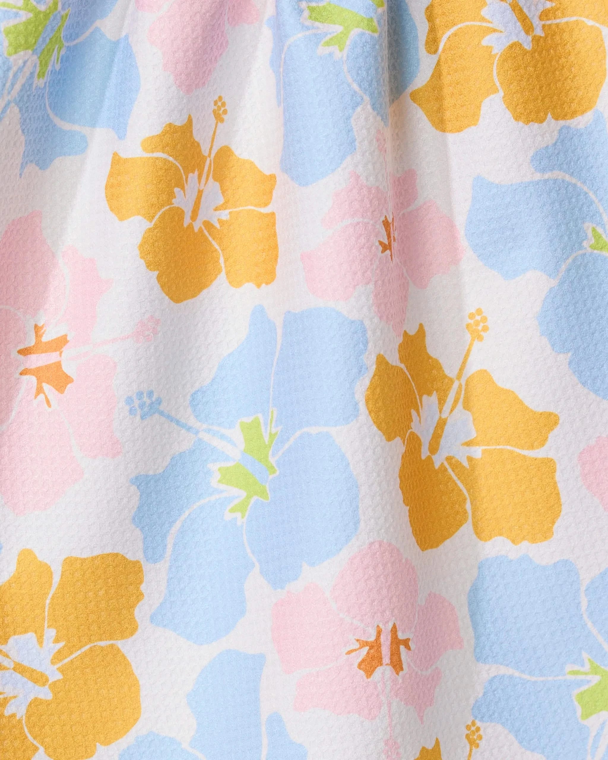 Close-up of the Hula Hues kitchen towel by GEOMETRY, made from eco-friendly fabric with large yellow, blue, and pink hibiscus flowers with light green centers on a white background.
