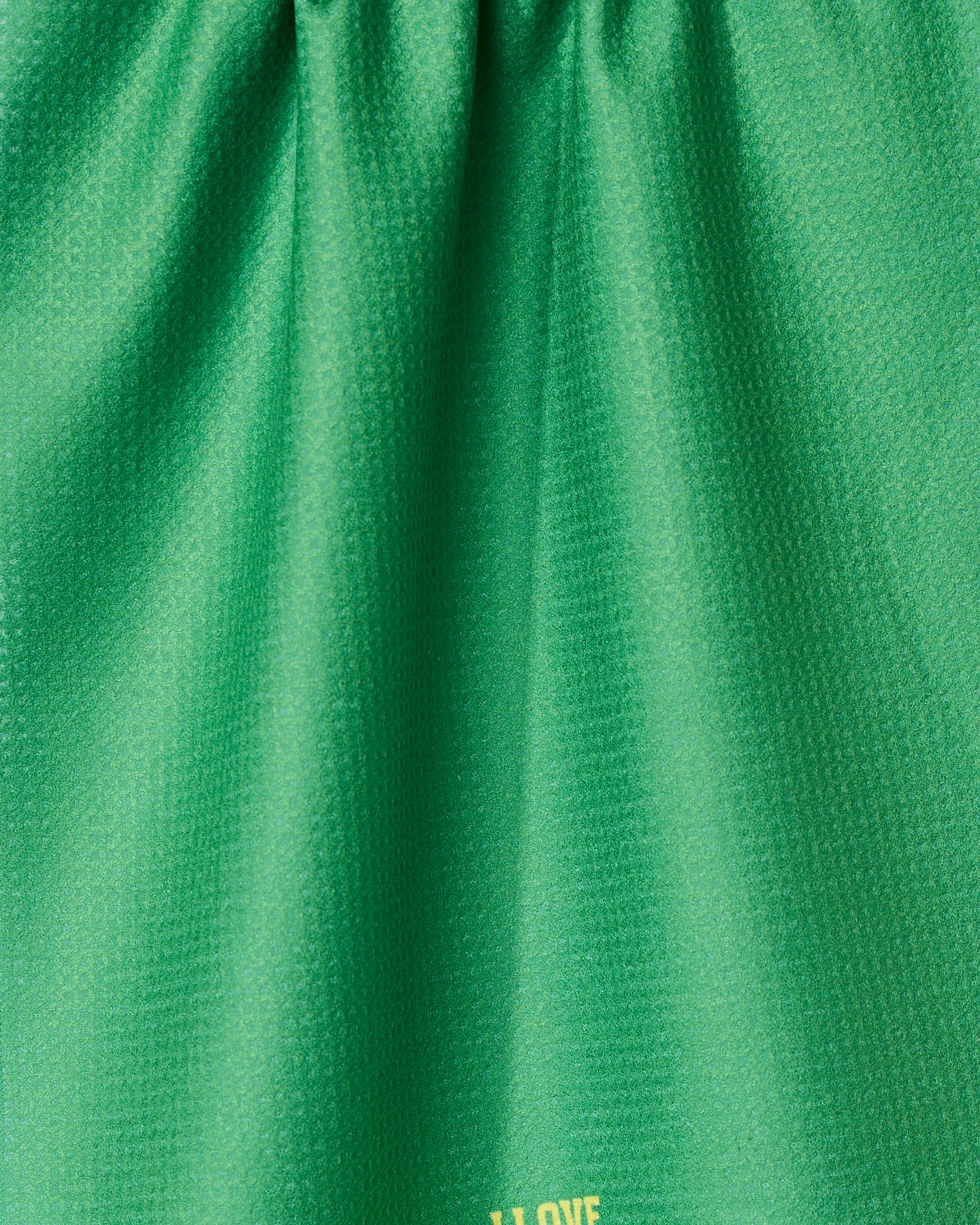 Close-up of a green, textured I Love Pickleball tea towel by GEOMETRY. Made from recycled materials, it has soft folds, a subtle sheen, and yellow text partially visible near the bottom edge.