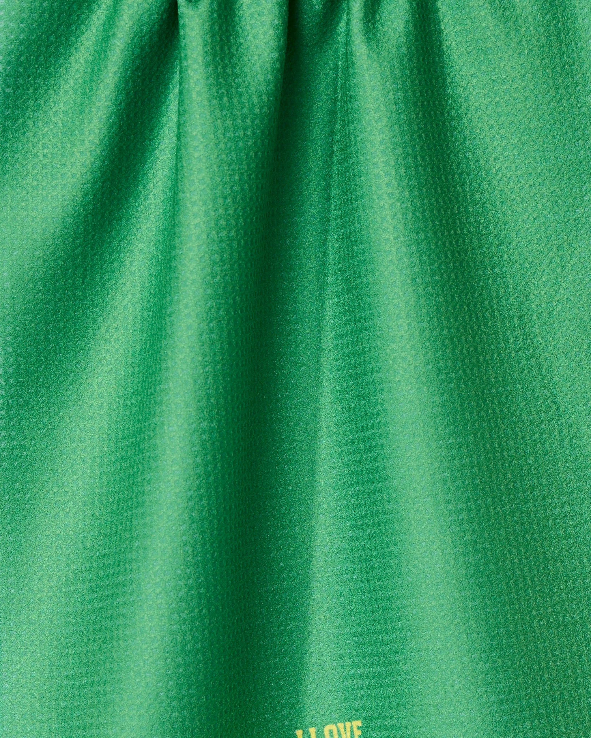 Close-up of a green, textured I Love Pickleball tea towel by GEOMETRY. Made from recycled materials, it has soft folds, a subtle sheen, and yellow text partially visible near the bottom edge.