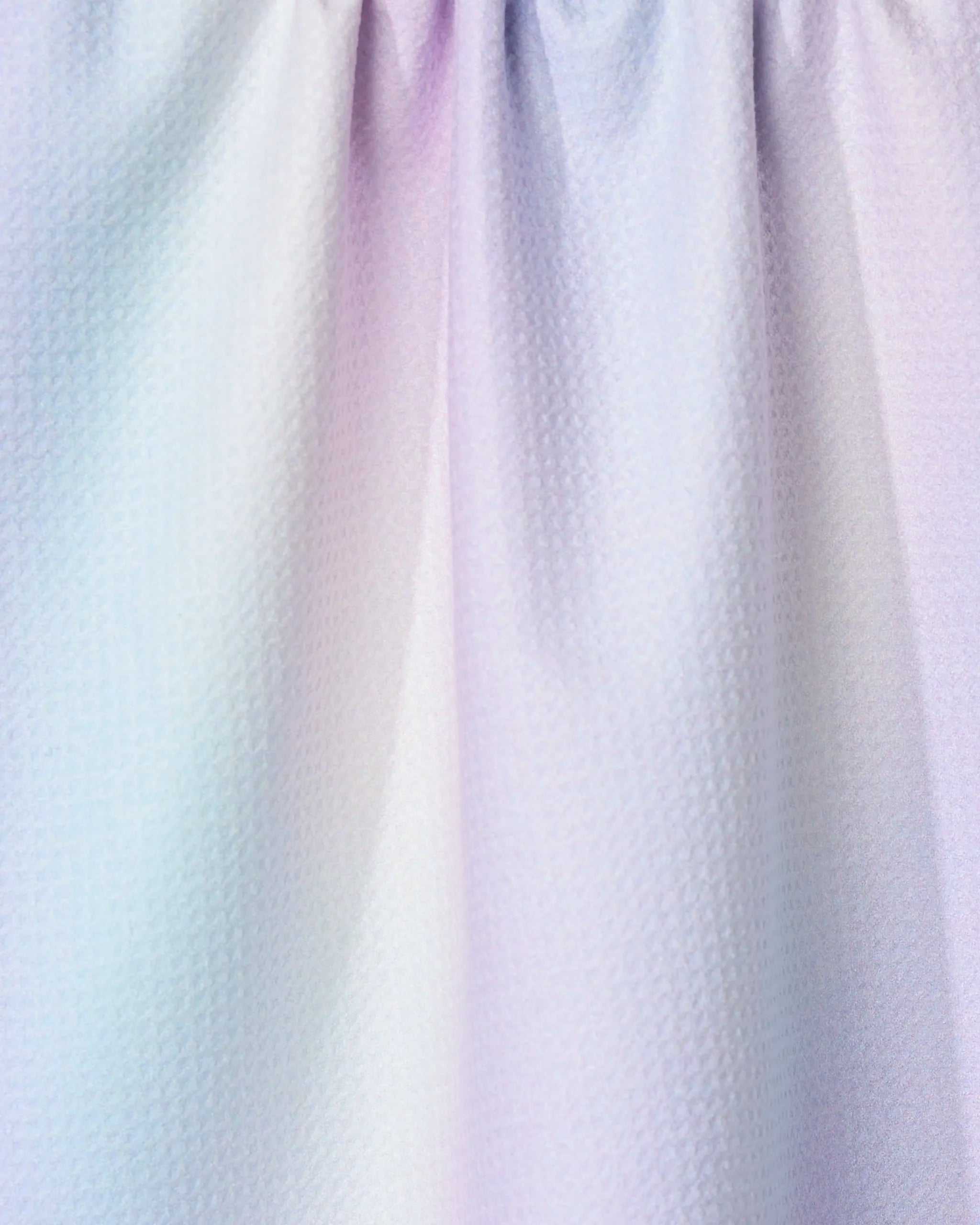 Close-up of the GEOMETRY Iridescence tea towel, featuring pastel hues of light blue, pink, and purple with a textured finish. The ultra-absorbent kitchen towel has soft folds and is gently gathered at the top.