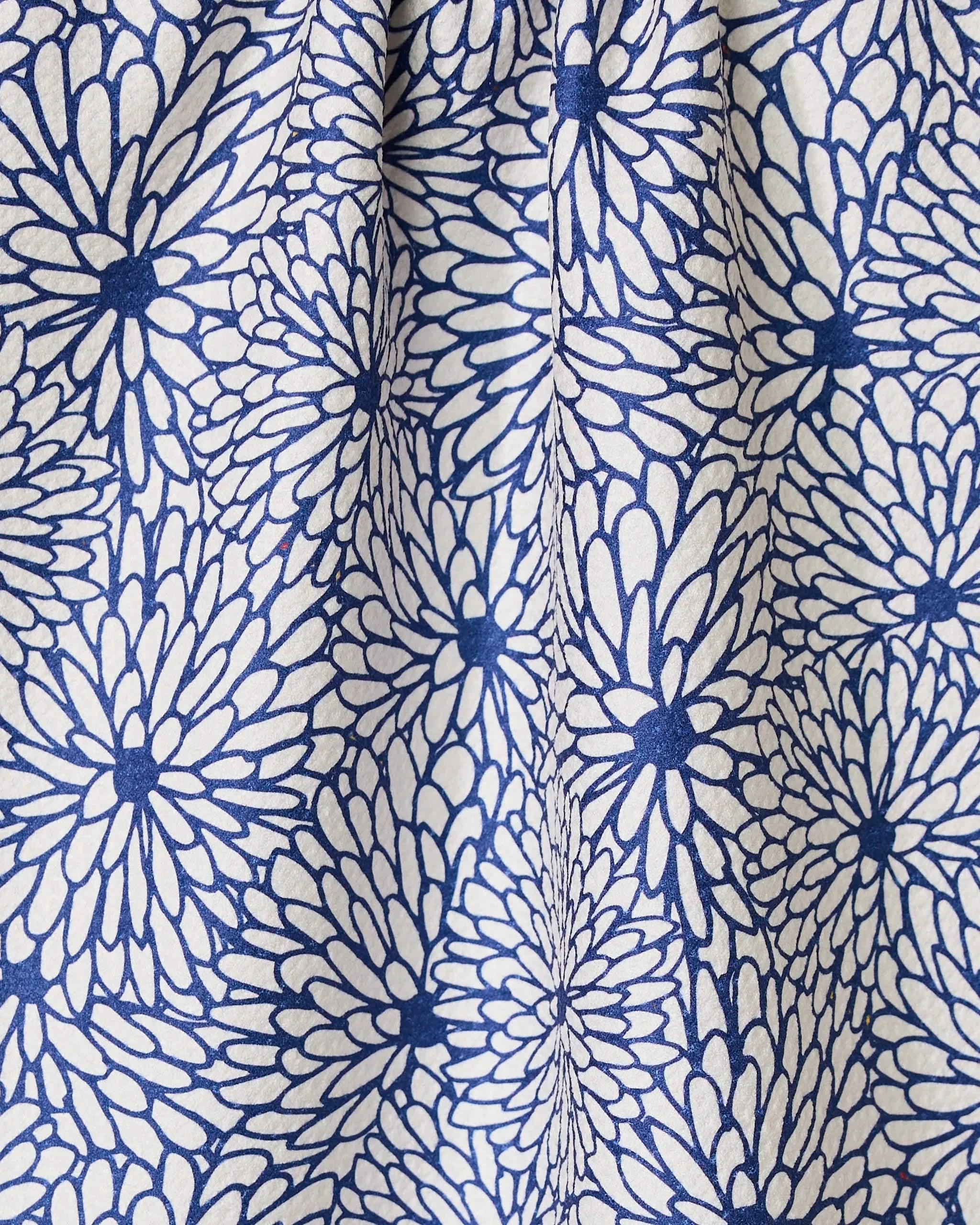 The GEOMETRY Jar Jar tea towel features white fabric with a repeating pattern of blue, daisy-like flowers. Made with super-absorbent Geoweave technology, its gentle folds create subtle shadows in the vibrant floral print.