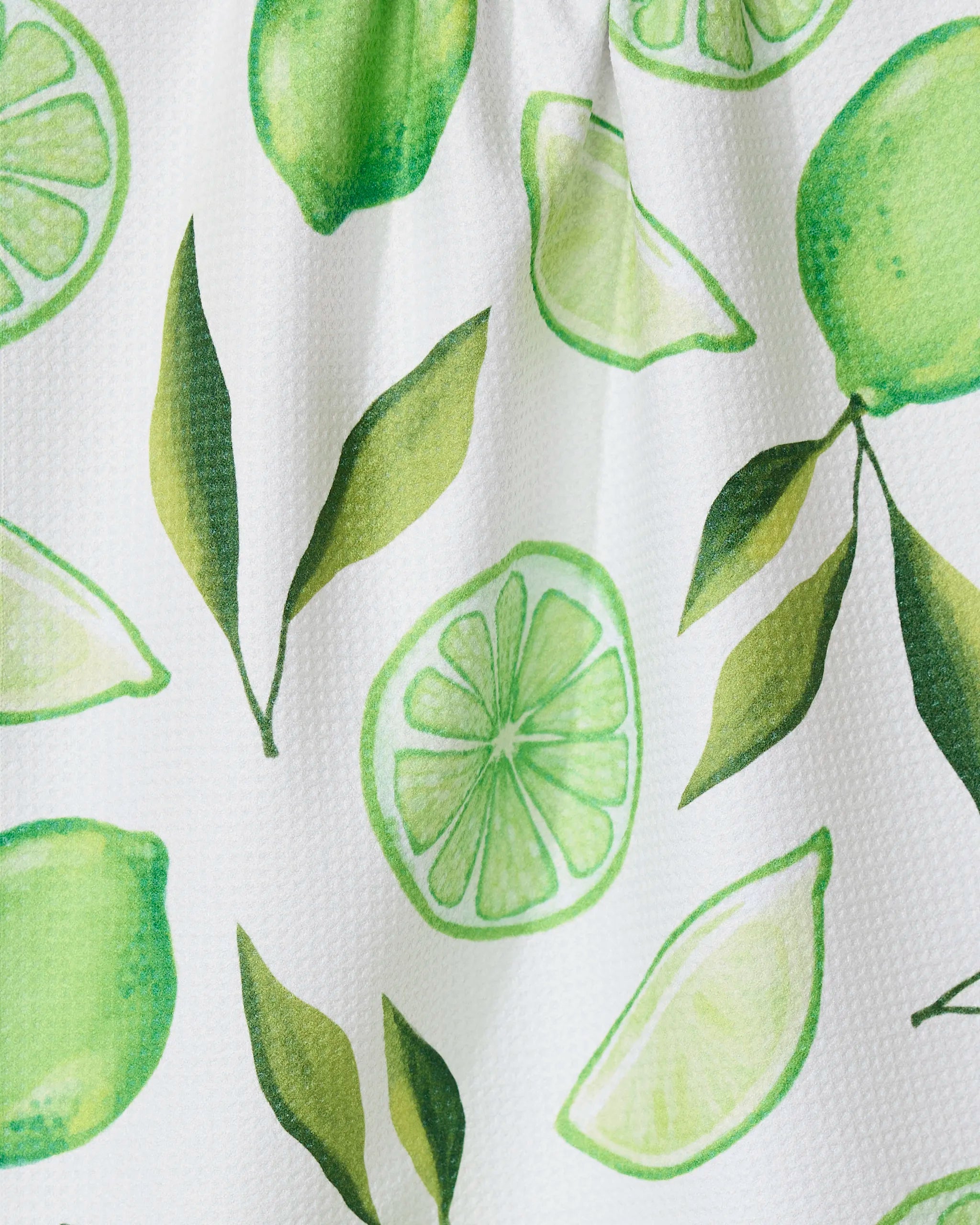 The GEOMETRY Lima kitchen towel features bright, watercolor-style limes, slices, wedges, and green leaves on a white textured background. Made from recycled materials.