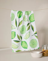 The GEOMETRY Lima kitchen towel, made from recycled materials and featuring green lime and leaf designs, hangs above a glass jar of brown sugar and a white bowl with a wooden spoon.