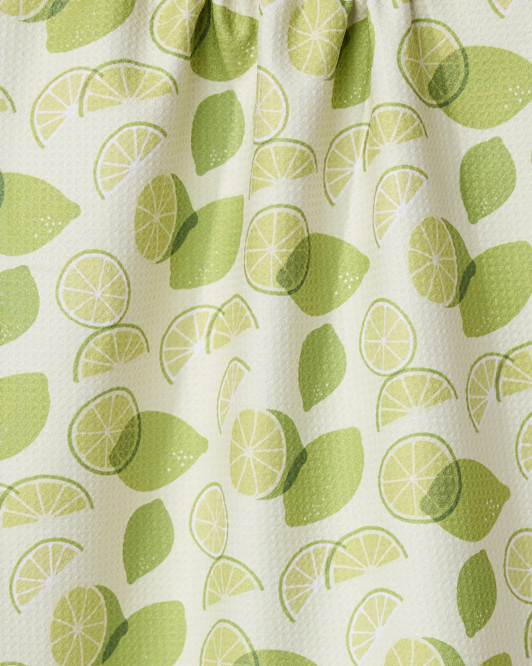 A close-up of the GEOMETRY Limes recycled kitchen towel, showing whole and sliced lime patterns in green on a light background. The fabric is slightly textured and gathered at the top.
