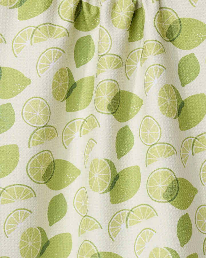 A close-up of the GEOMETRY Limes recycled kitchen towel, showing whole and sliced lime patterns in green on a light background. The fabric is slightly textured and gathered at the top.